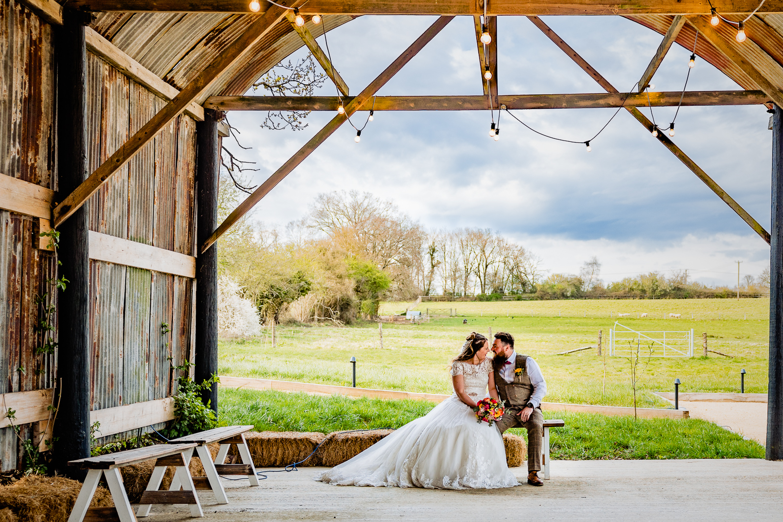 bride and groom sitting on a bale of straw in a dutch barn at silchester farm