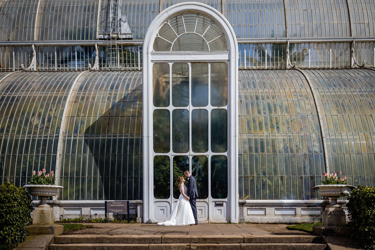 Bride & groom pose facing each other in front of the door to the Palm House