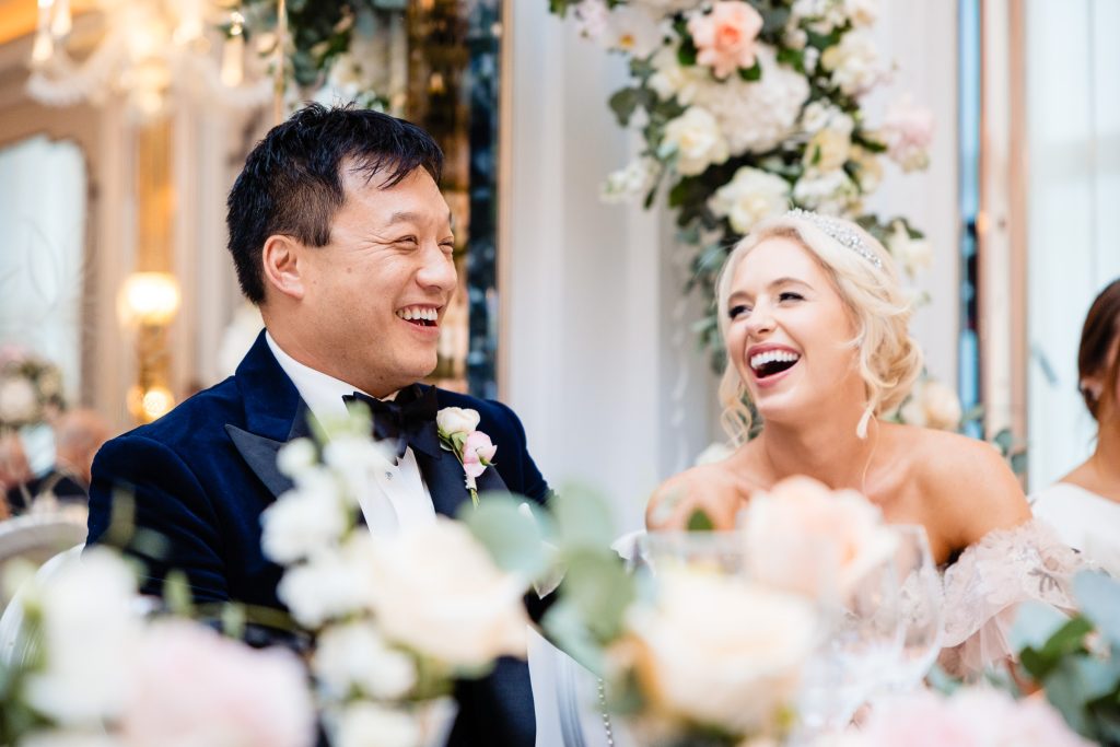 Bride & groom laugh together at their wedding reception in Claridges ballroom, London