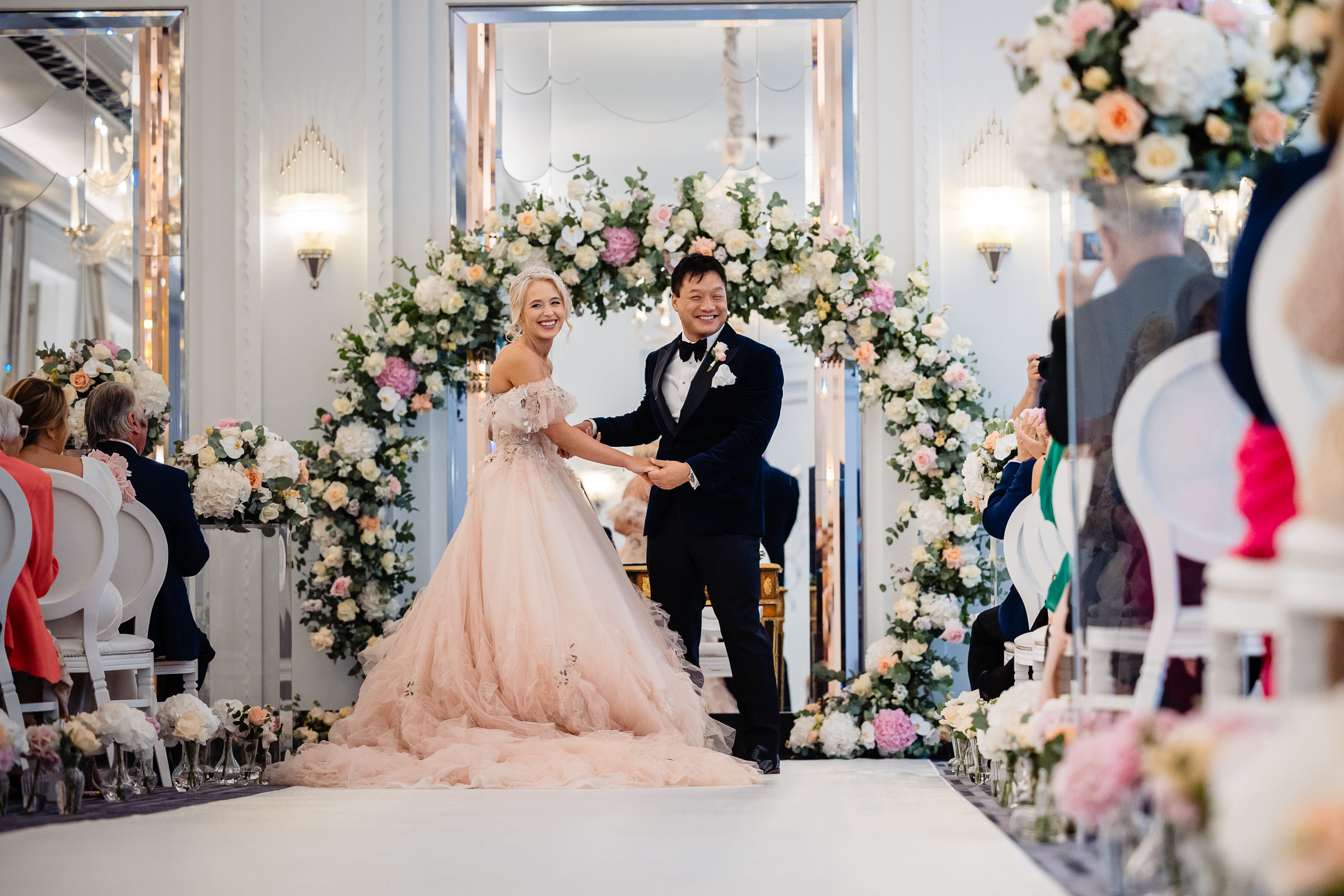 Photograph by Beautifullight UK photography of laughing bride wearing a pink dress & a laughing groom holding hands during their wedding ceremony at Claridges Hotel, London