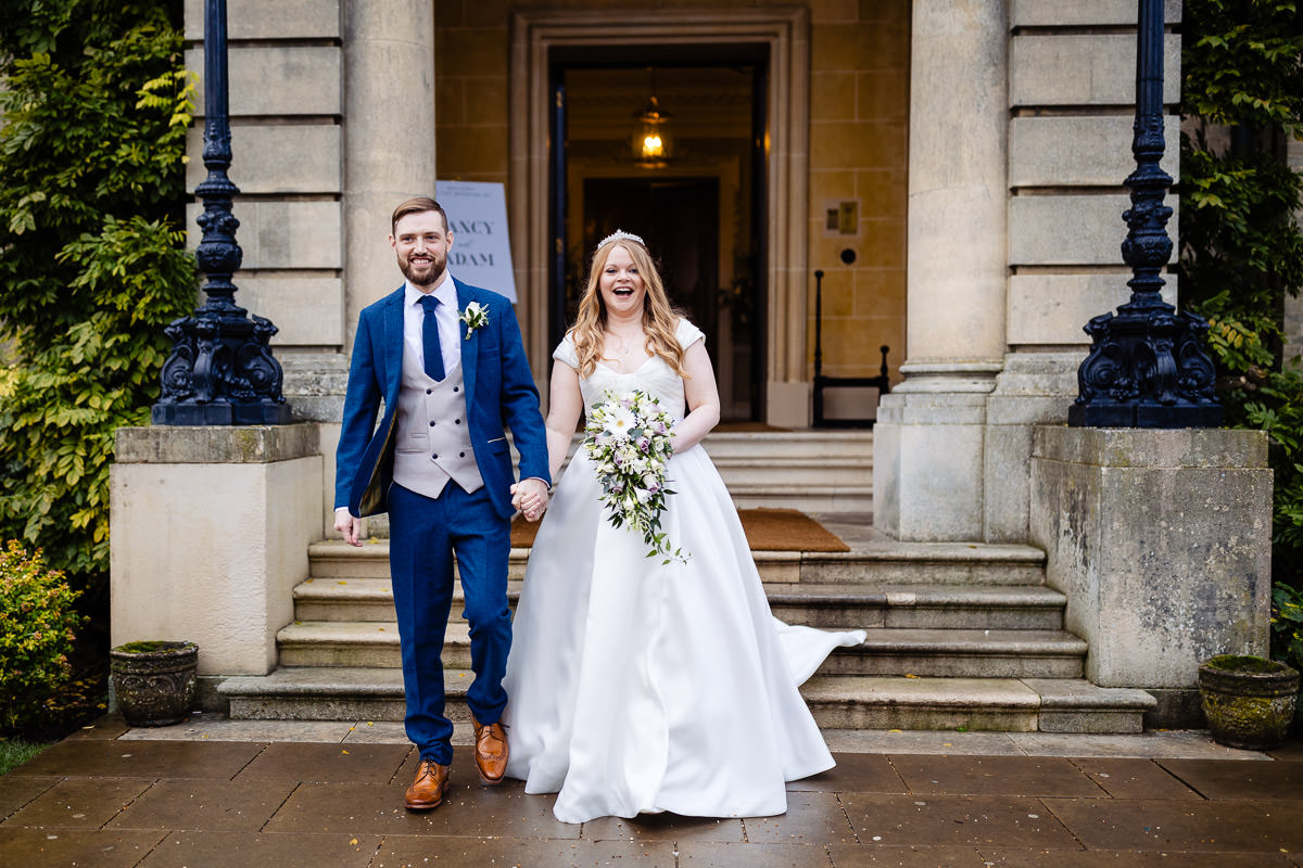 Bride & groom holding hands walking away from the front entrance to Hedsor House