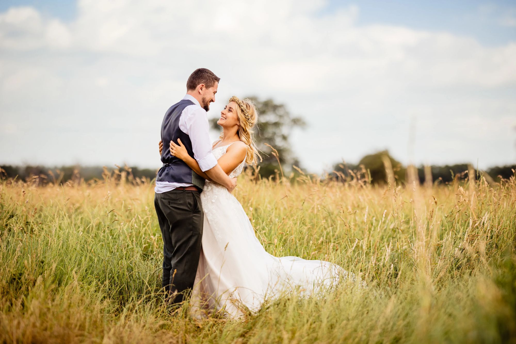 Bride wearing a flower crown embraces her groom in a field of long grass