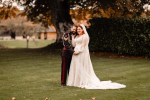 Newlywed couple on the lawns at Clock Barn. Smiling for a photograph by Beautifuyllight Photography