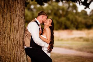 Newlywed couple embrace under a tree at De vere Wokefield Estate. Laughing & naturally relaxed during a photoshoot with Beautifullight Photography