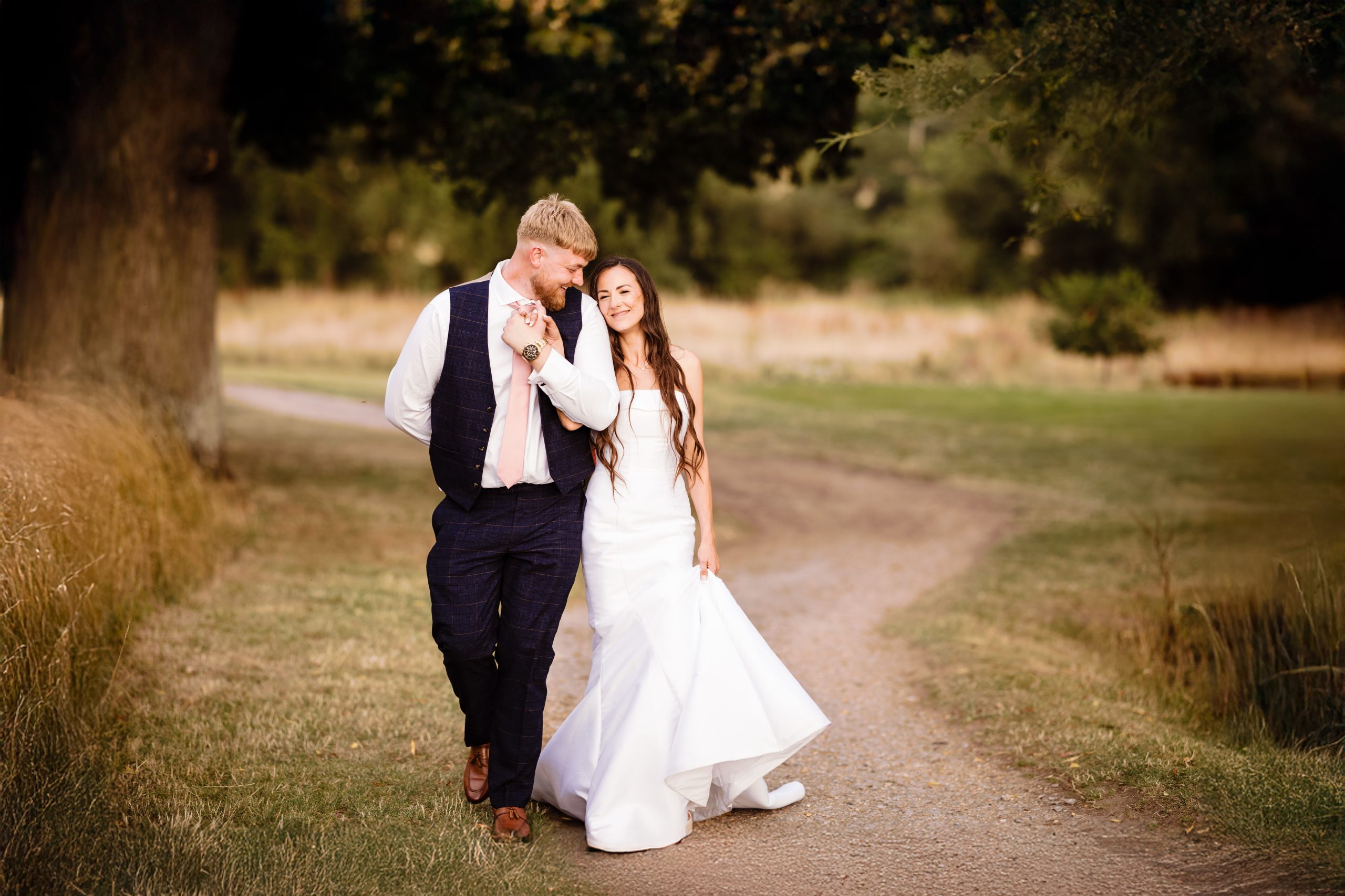 A smiling Bride & groom walk naturally together holding hands in the grounds of Wokefield estate